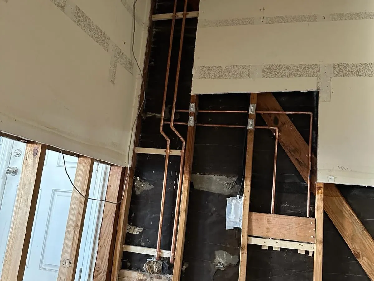 Drywall cut away to show new copper water lines running up and across the wall framing