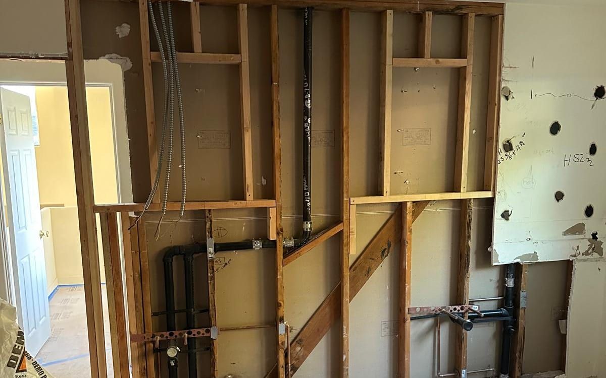 A wall opened down to the framing in a gutted room, showing new drain and water rough-ins on both sides